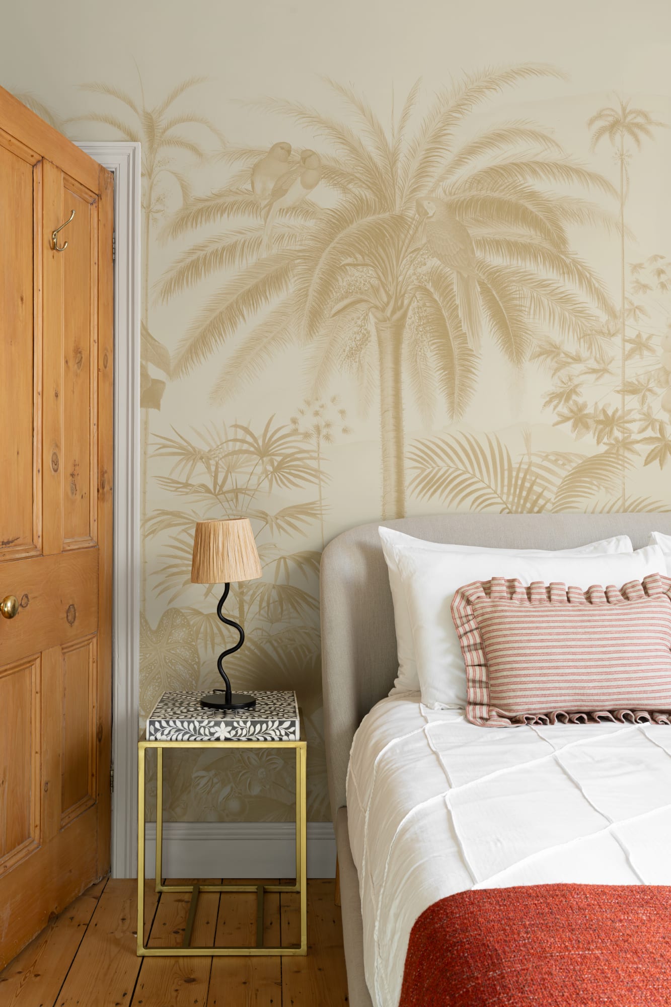 Bedroom with a beige tropical palm mural and a neutral upholstered bed with a striped cushion.