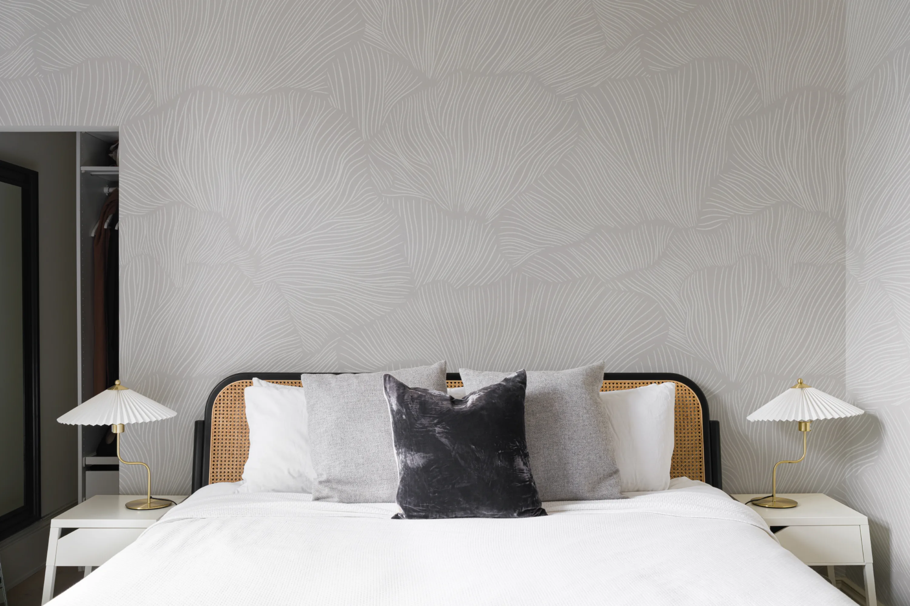 A softly patterned gray wallpaper with large leaf-like shapes behind a modern bed with monochrome cushions.