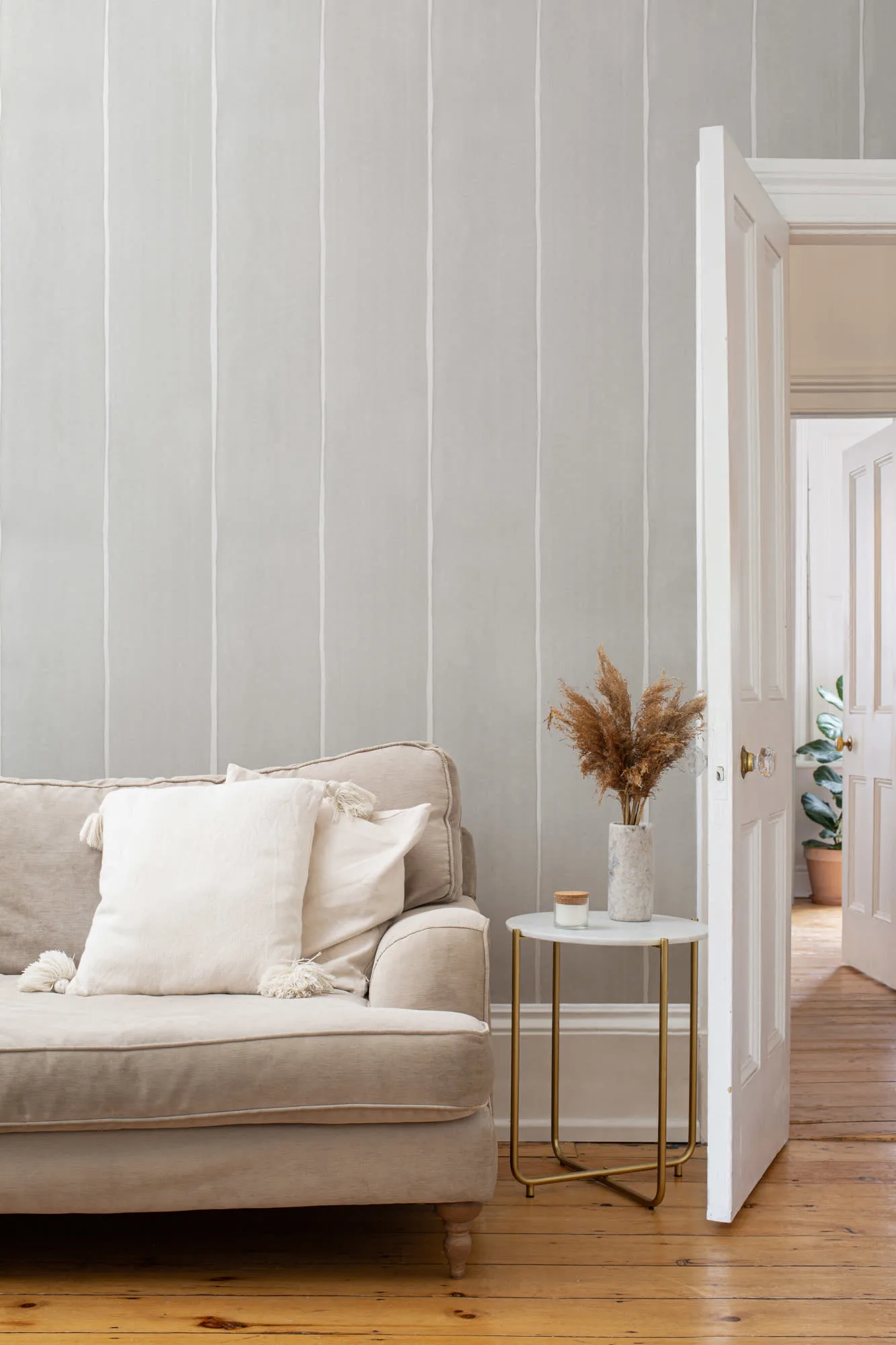 A light gray wall with soft vertical painted stripes in a cozy living room with a beige sofa and white pillows.