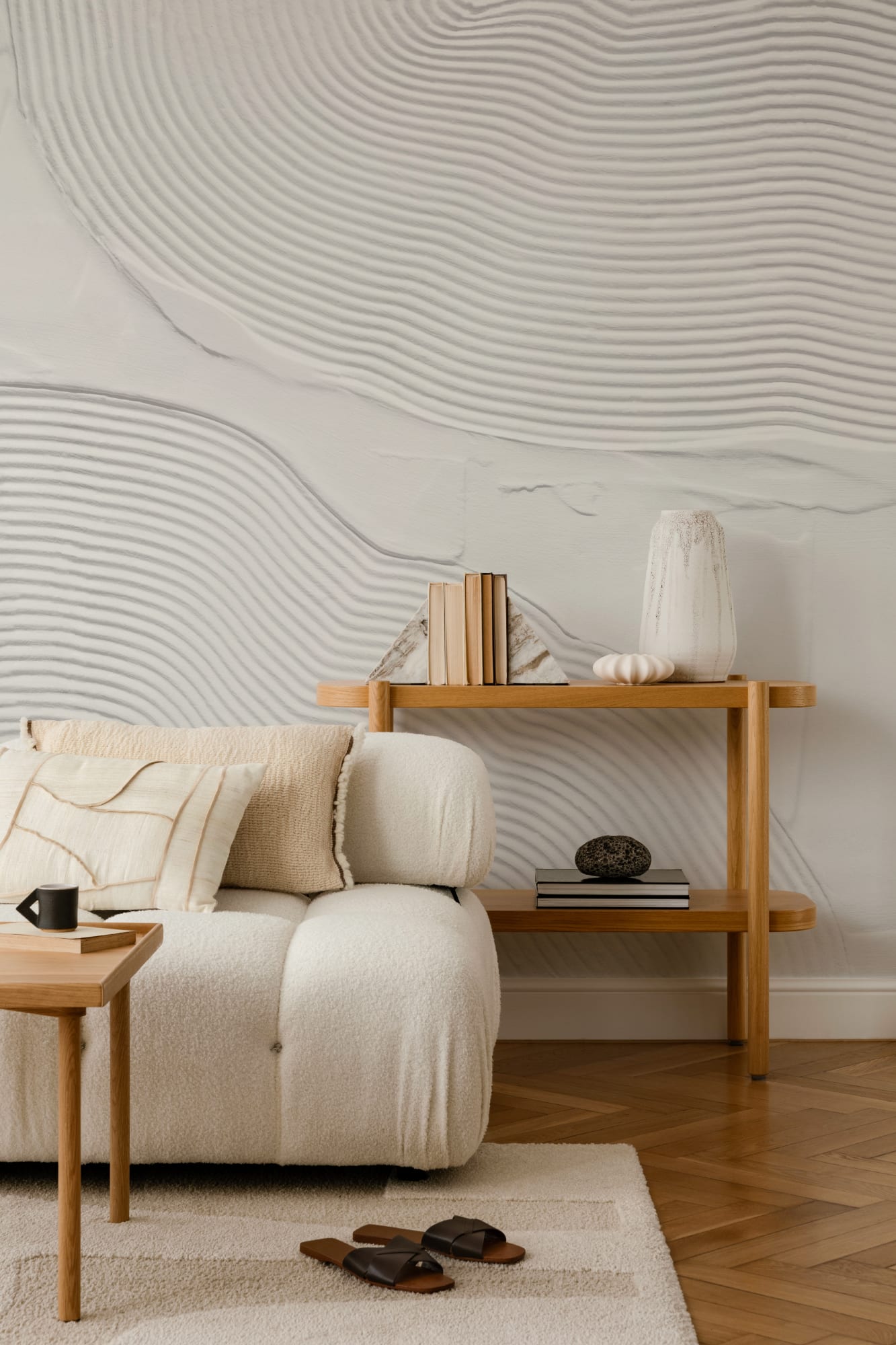 A textured wall mural with sculptural, sand-like wave forms behind a cream sofa and wood console table.