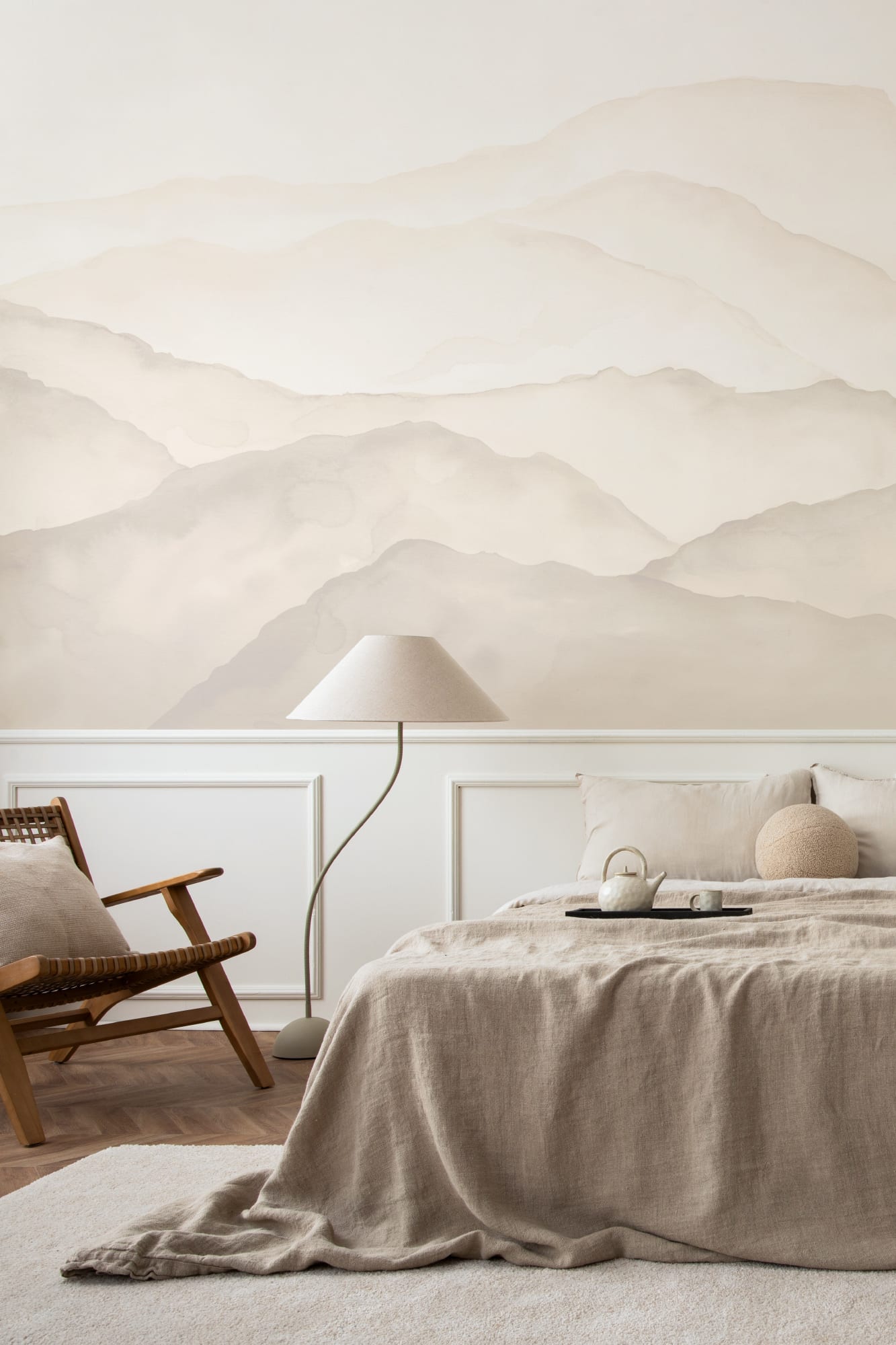 A watercolor mountain mural in soft beige tones behind a bed with linen bedding and natural decor.