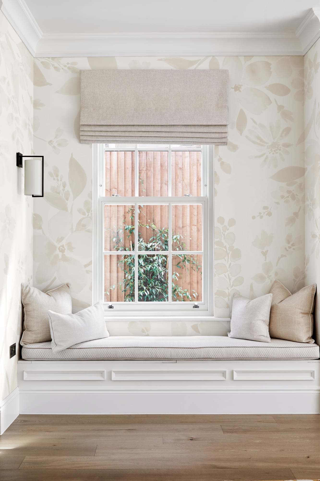 Window seat with cushions against walls covered in neutral floral wallpaper in a soft, beige tone.