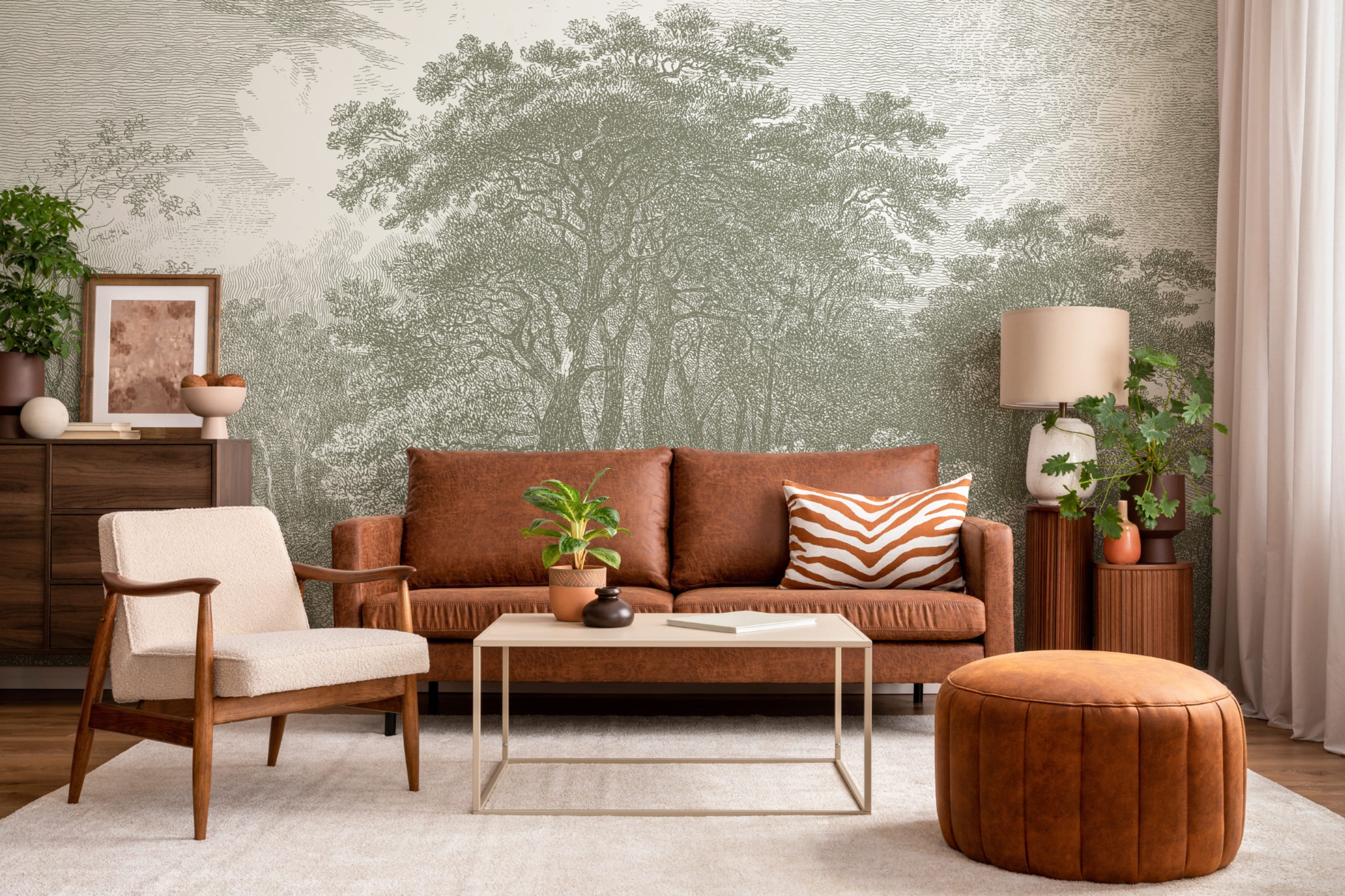 Living room with a green illustrated forest mural, brown leather sofa, and mid-century decor.