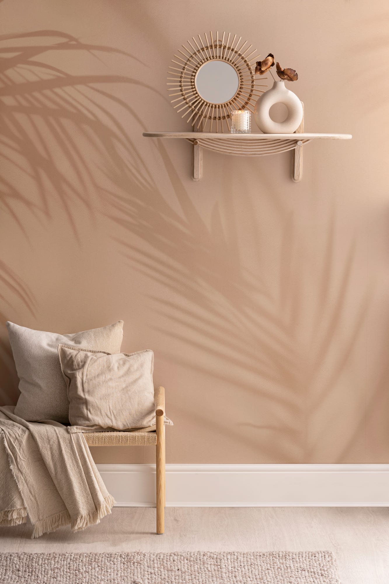 Palm leaf shadows on warm peach wall behind a bench with neutral pillows and blanket.