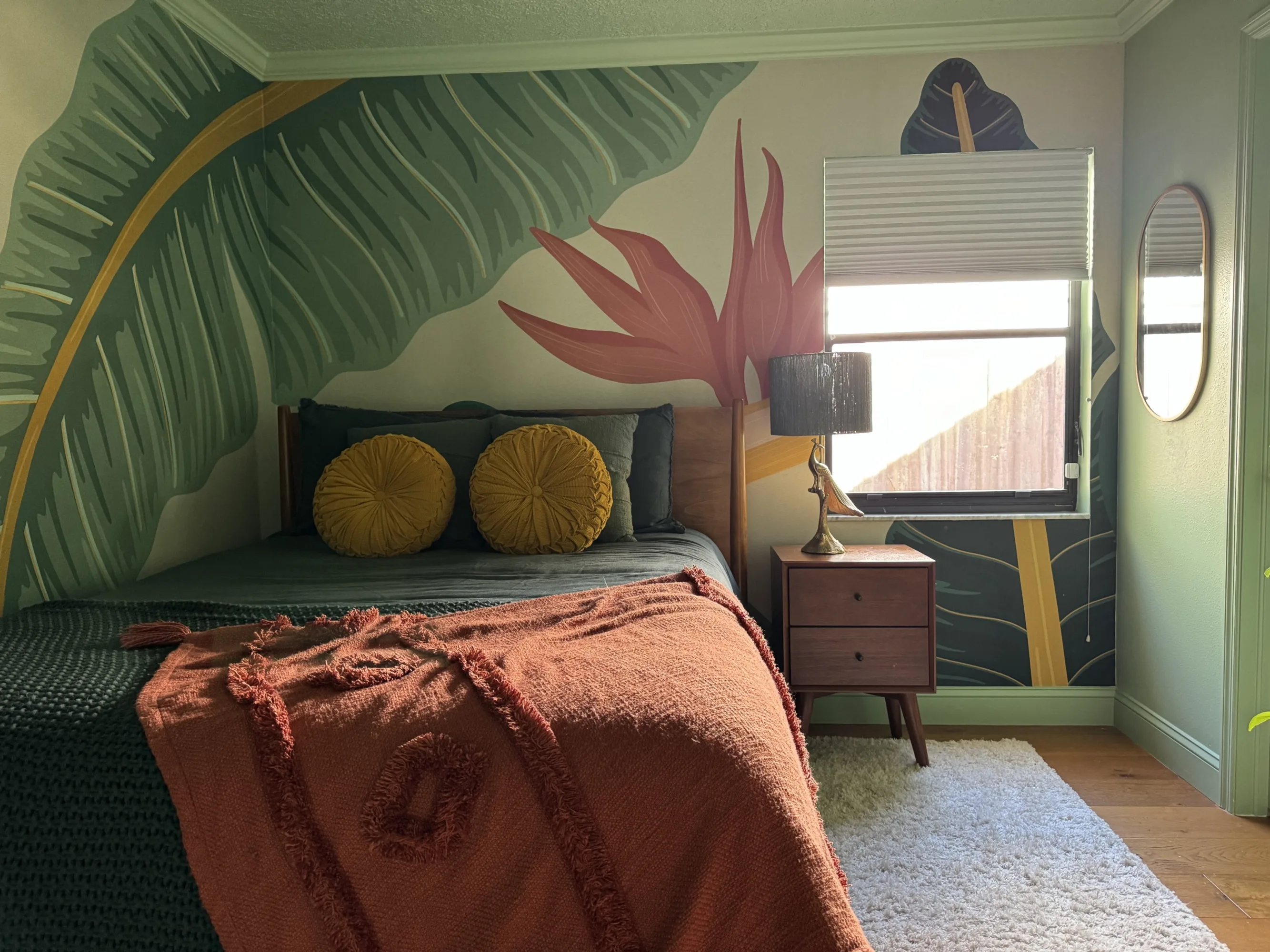 Bedroom with bold tropical mural of large banana leaves and a red-orange throw.