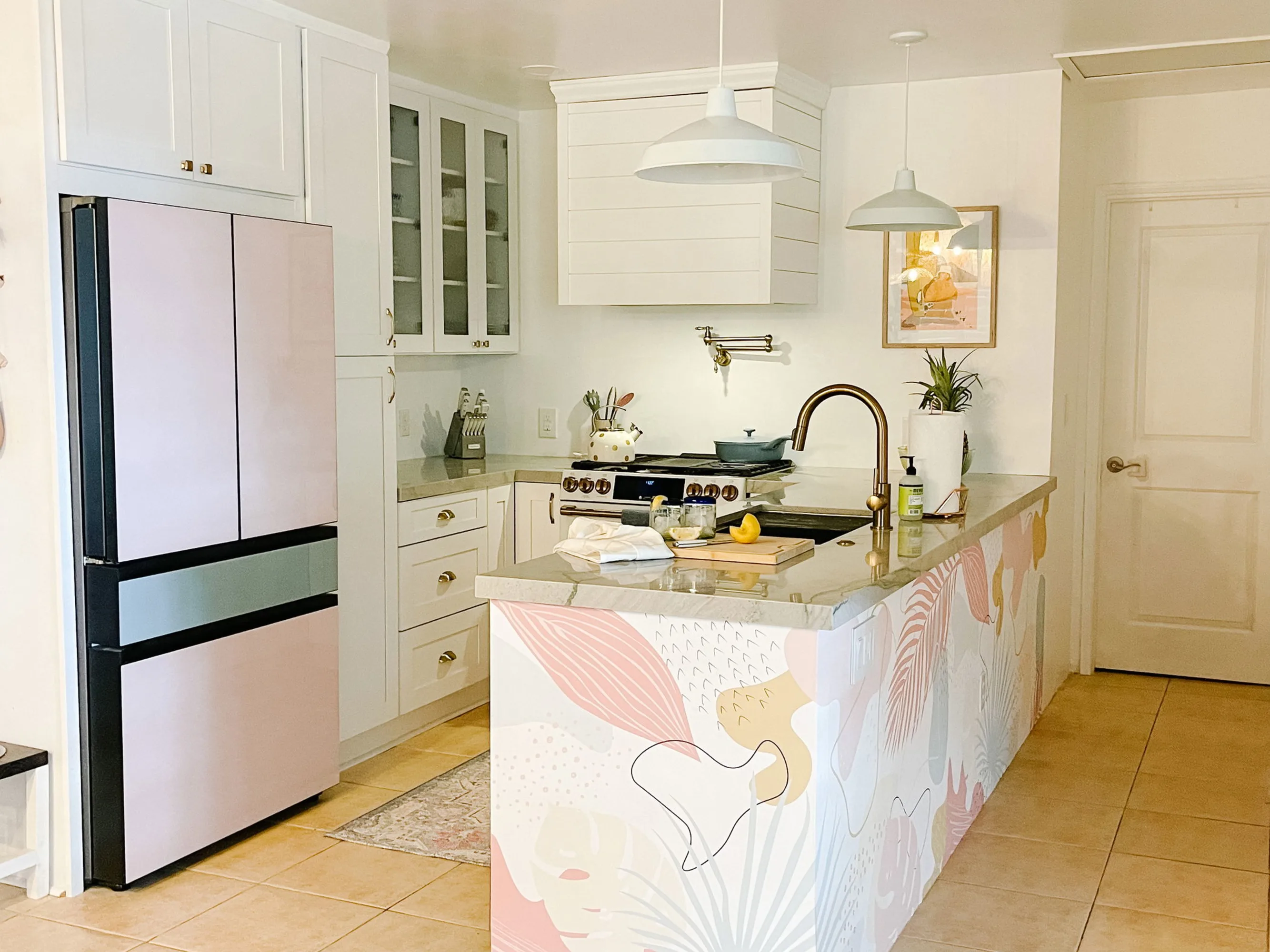 White kitchen with tropical pastel wallpaper wrapping around the island and pink refrigerator.