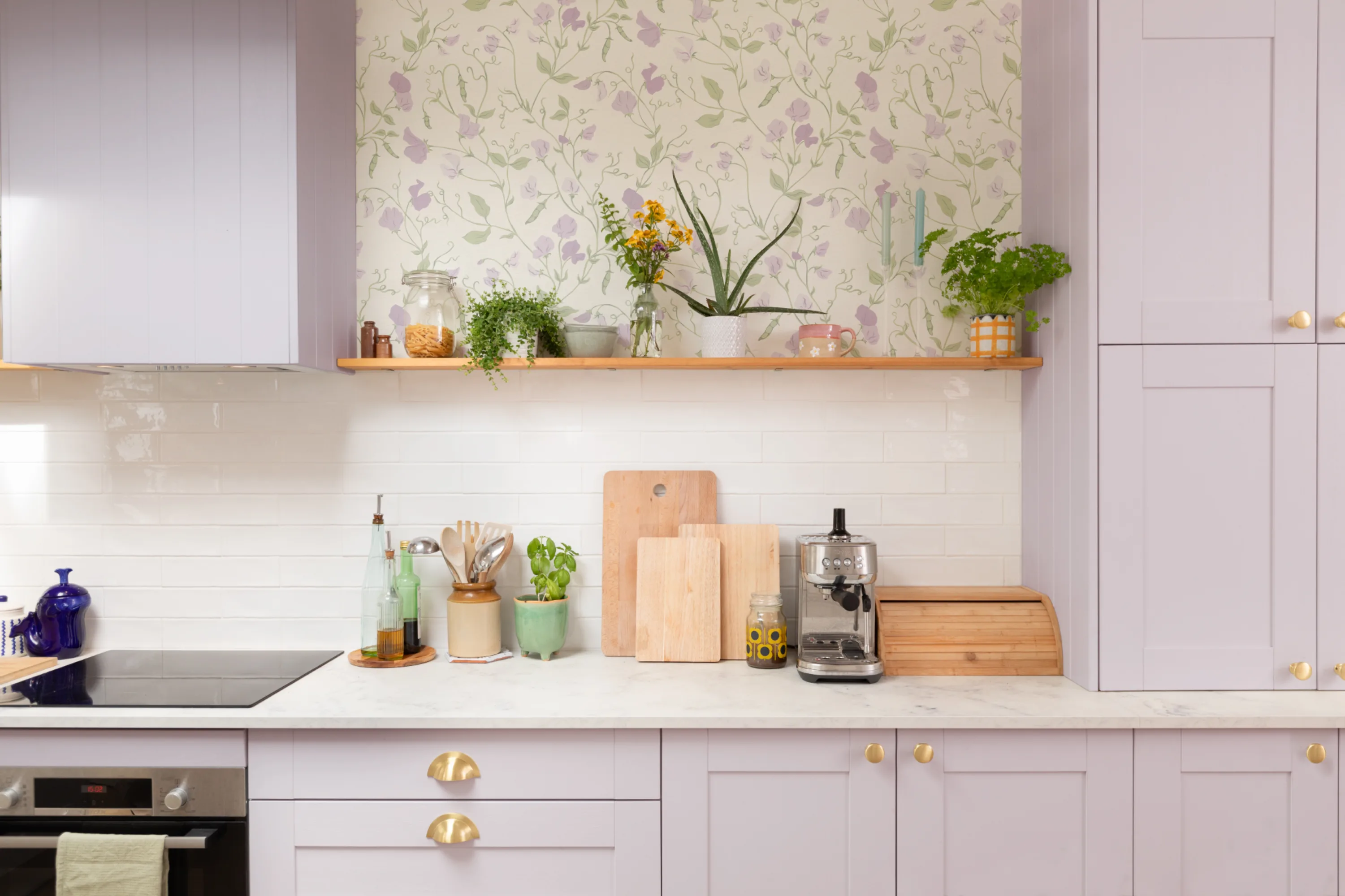 Lilac kitchen with green and purple floral wallpaper above a white tile backsplash.