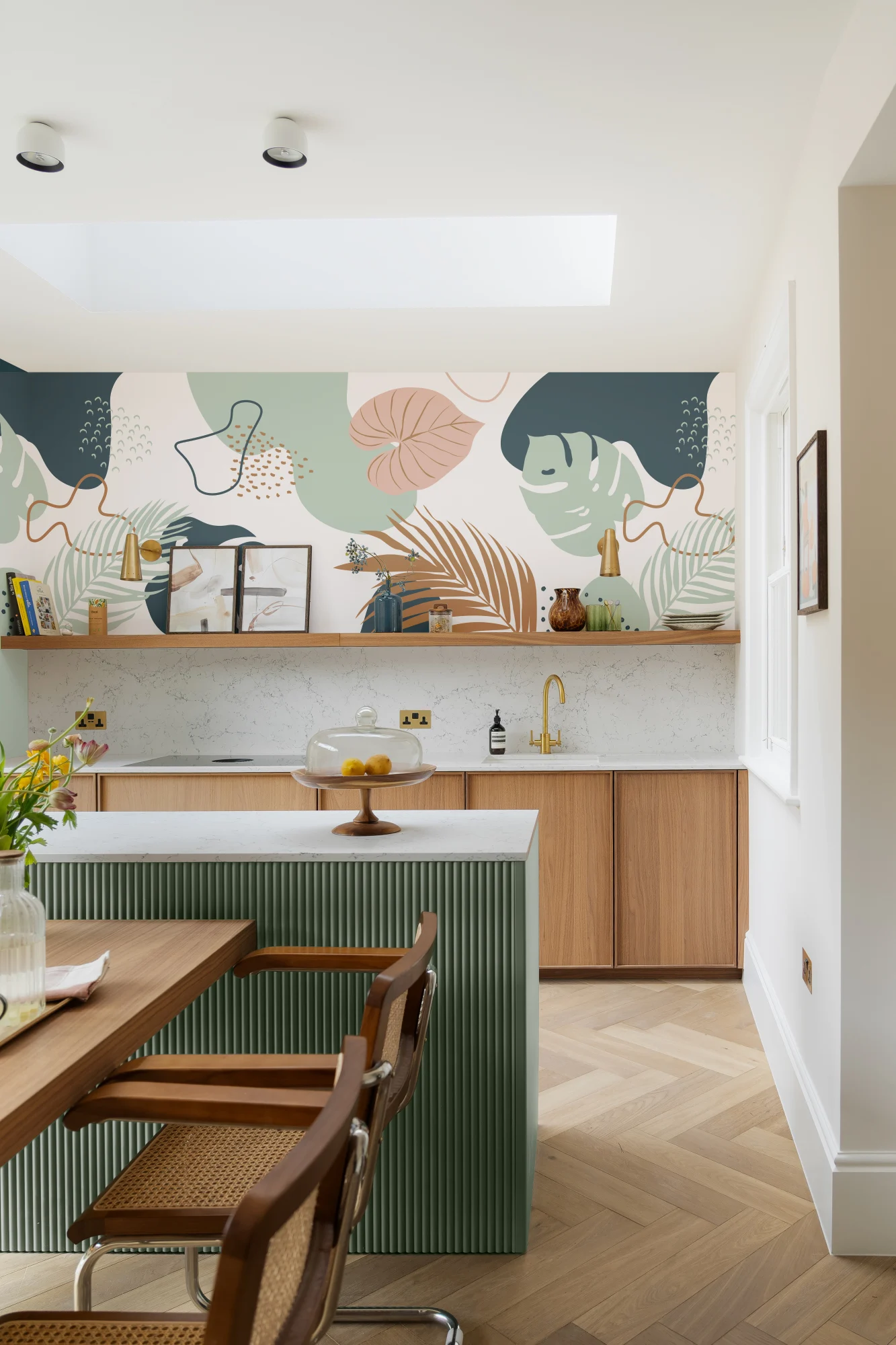 Bright kitchen with abstract tropical wallpaper in soft greens, peach, and navy over wooden cabinets.
