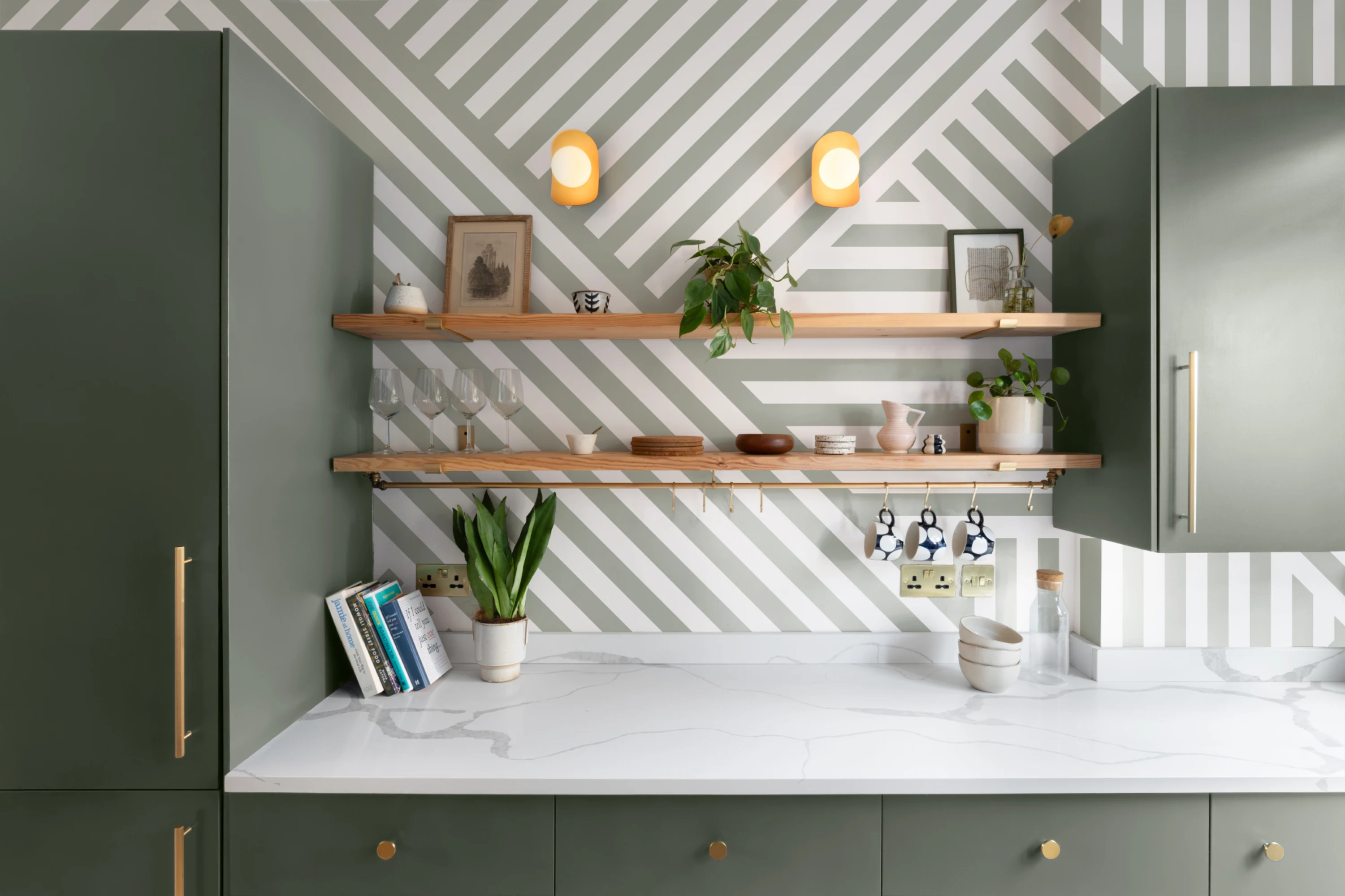 Open shelving kitchen with sage green cabinets and diagonal striped wallpaper in white and gray.