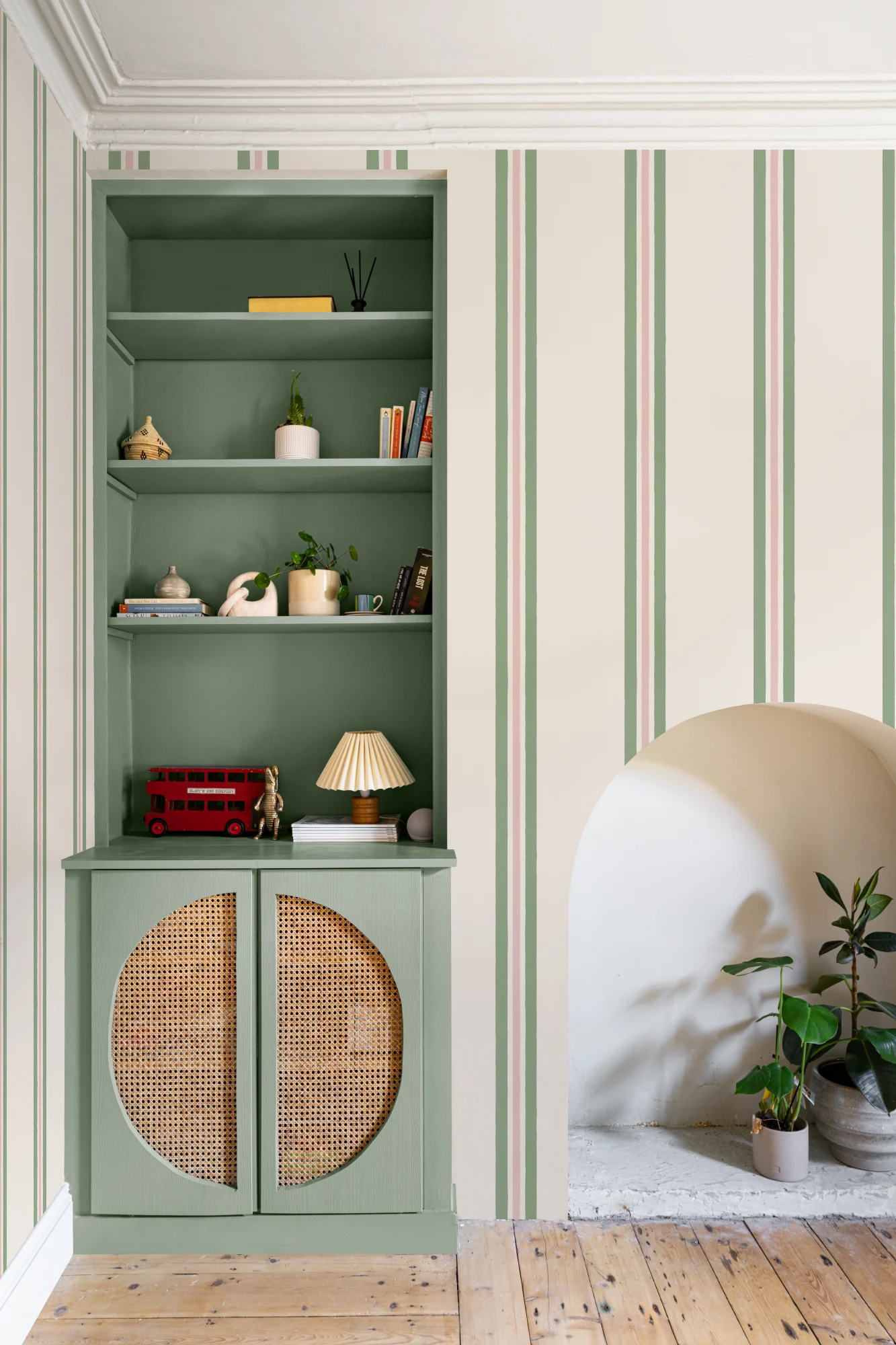 Built-in sage green shelving next to walls covered in vertical green and pink striped wallpaper.