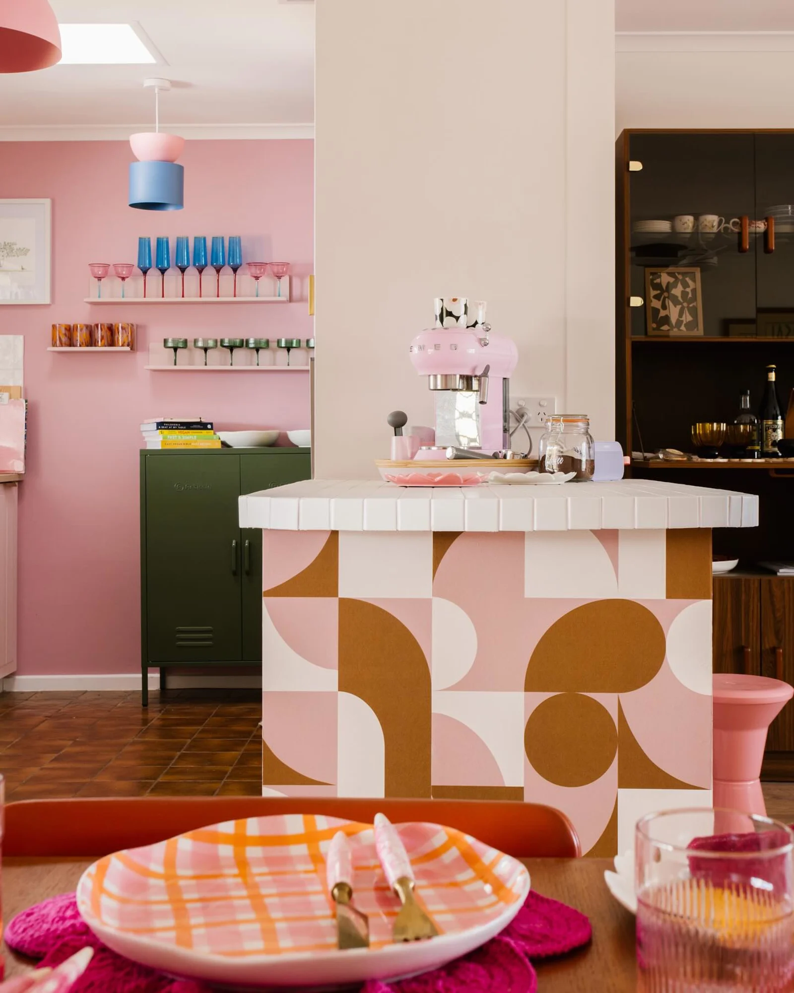 Pink and mustard geometric wallpaper on a tiled kitchen island in a colorful, retro-style kitchen.
