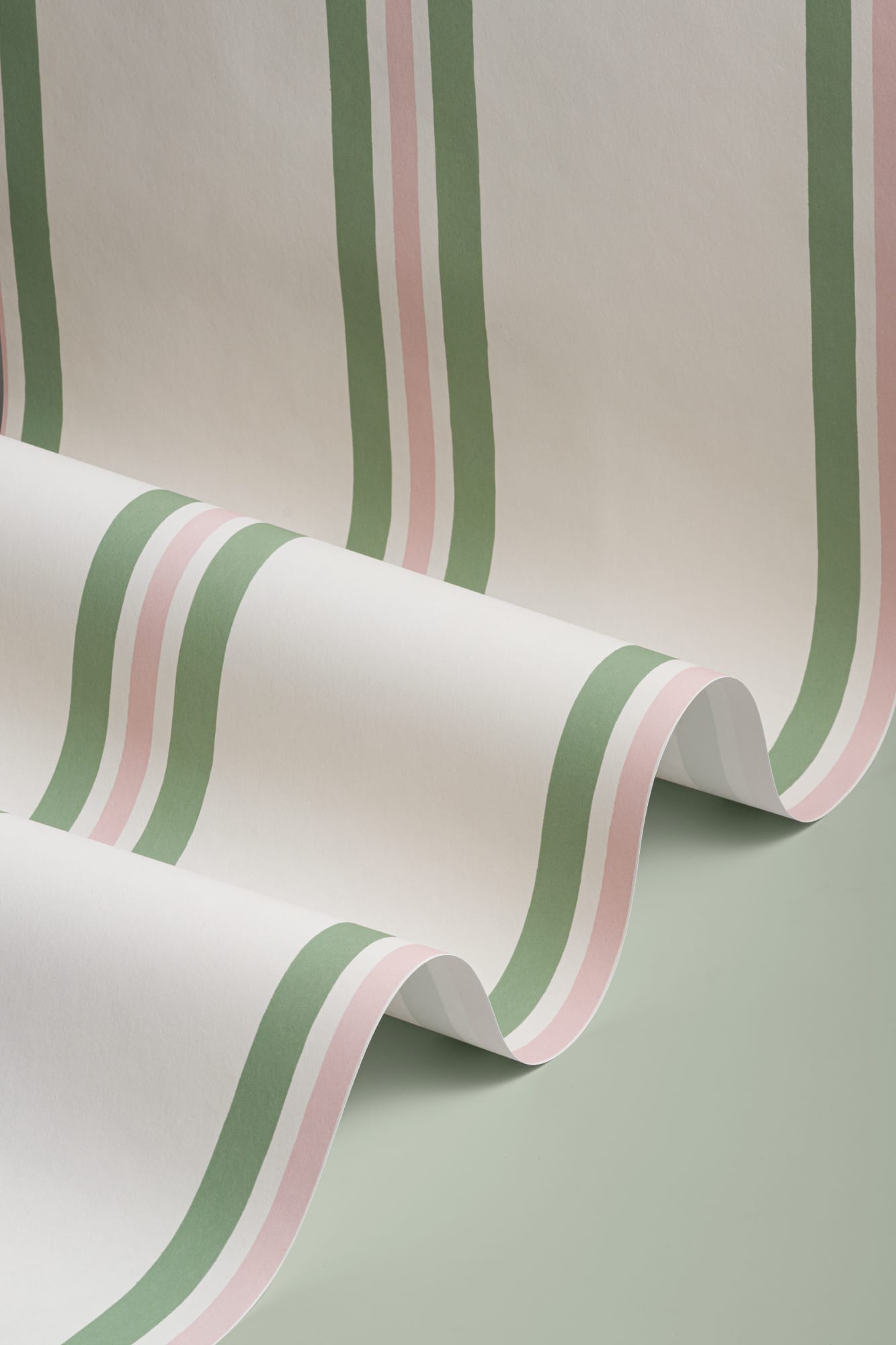 Close-up of a rolled wallpaper featuring wavy vertical stripes in sage green and pale pink on white.
