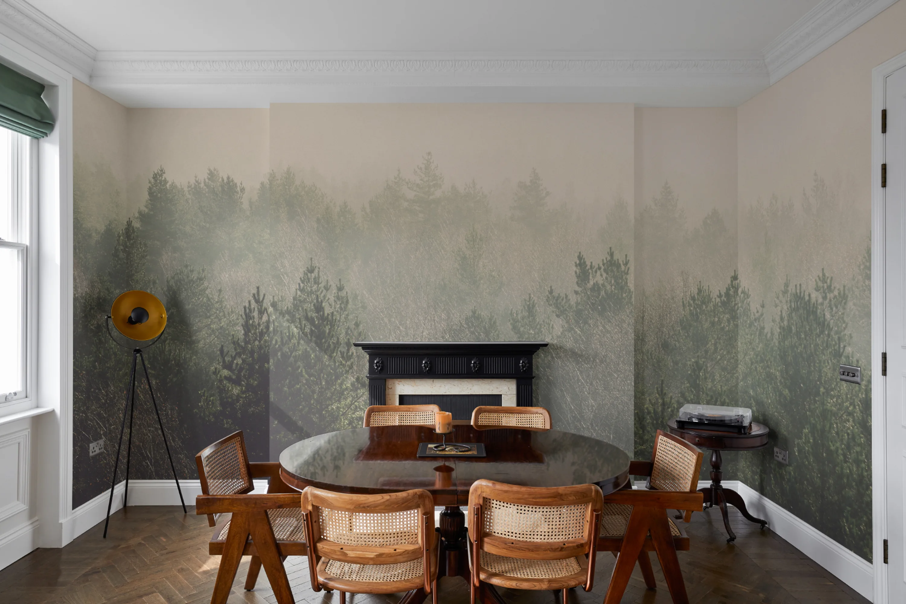 A misty green forest wallpaper creates a calming backdrop in a dining room with mid-century furniture and a black fireplace