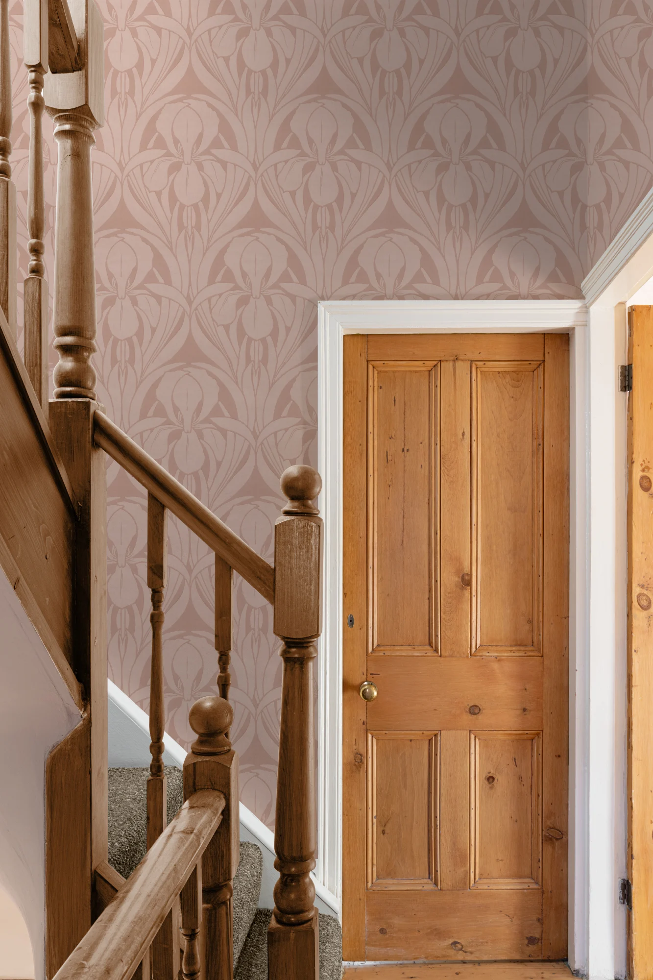 Pink Art Nouveau-style wallpaper in a hallway with a wooden staircase and door.
