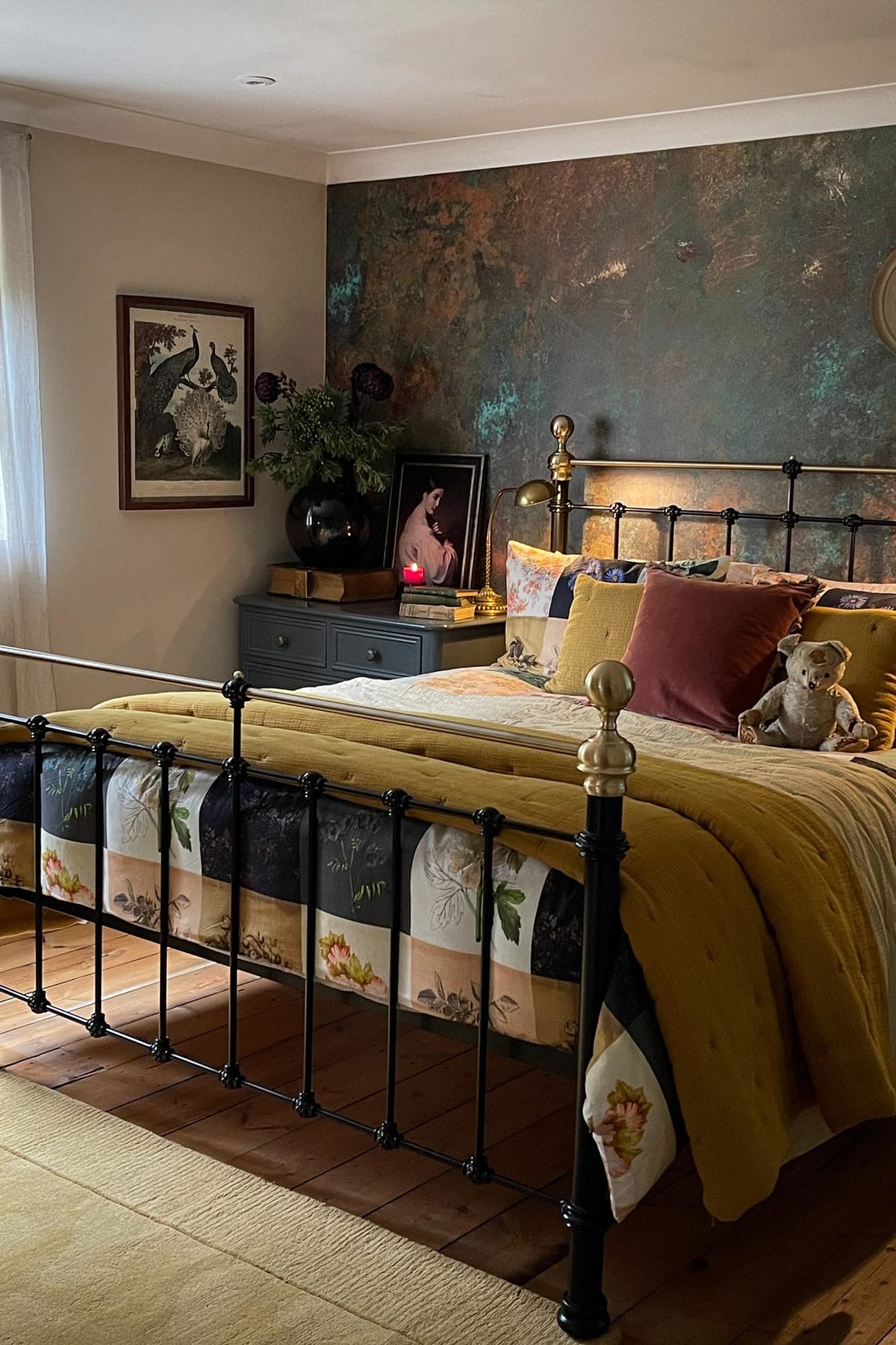 A bedroom with a distressed wall mural in dark earthy tones and a vintage black iron bed.