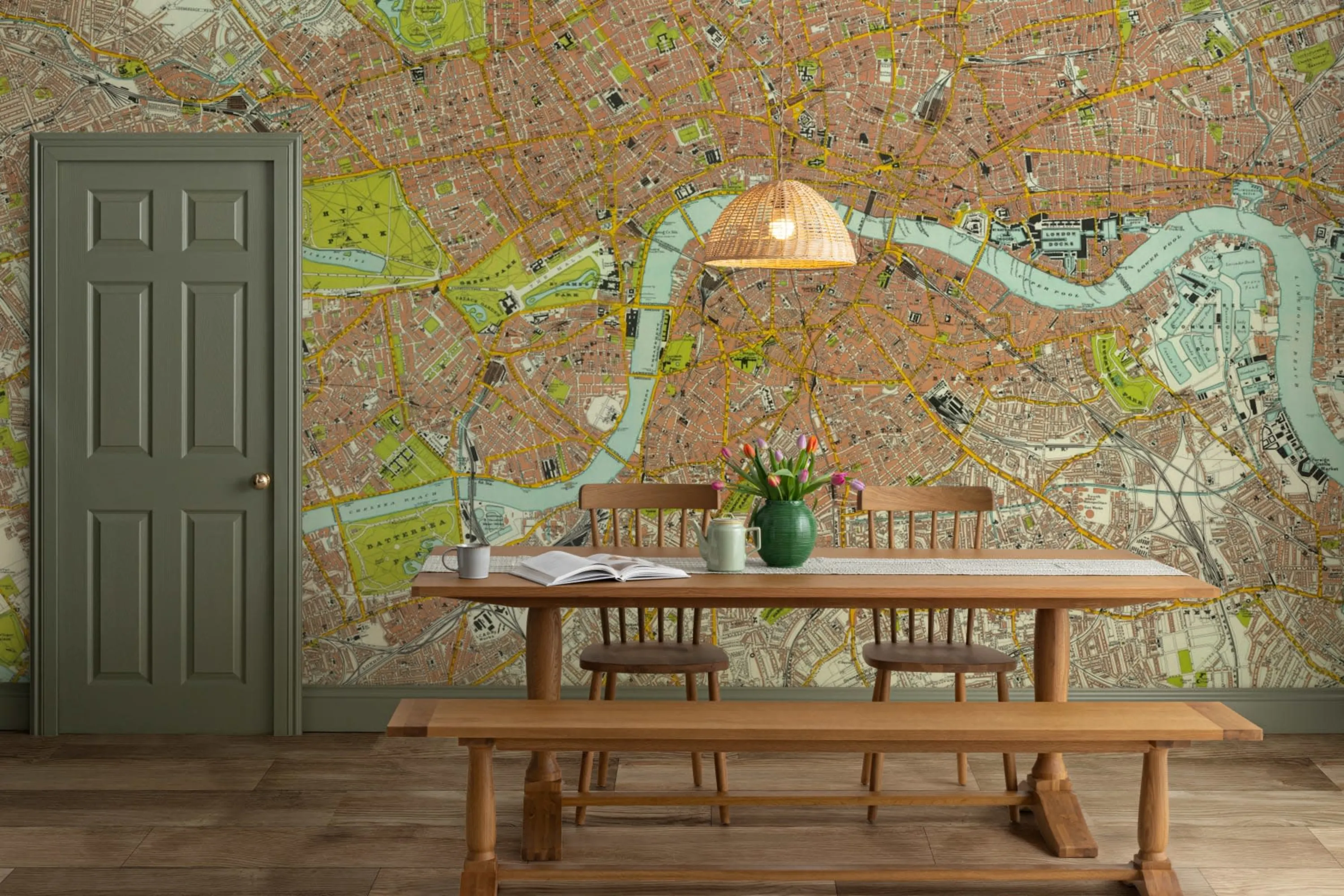 A dining area with a wooden table and bench set, green door, and a wallpaper mural featuring a detailed map of a city, accented by a hanging wicker light fixture.